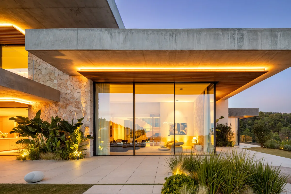 Terrasse d'une villa contemporaine à la tombée du jour, baies vitrées éclairées.